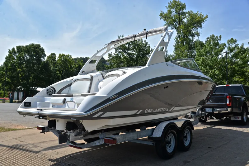 Slide: The Image of 2015 Yamaha Boats 242 Limited S on trailer, parked outdoors with trees in background. - 13