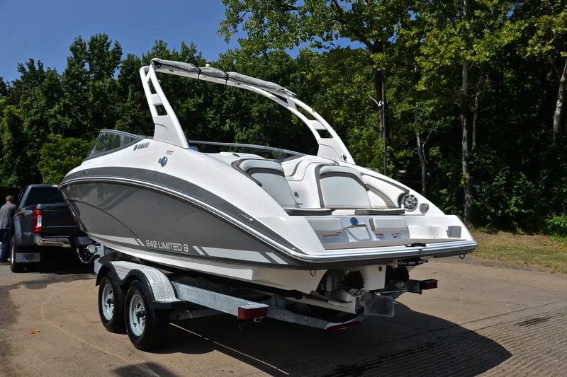 Slide: The Image of 2015 Yamaha Boats 242 Limited S on trailer, parked near lush green trees. - 11