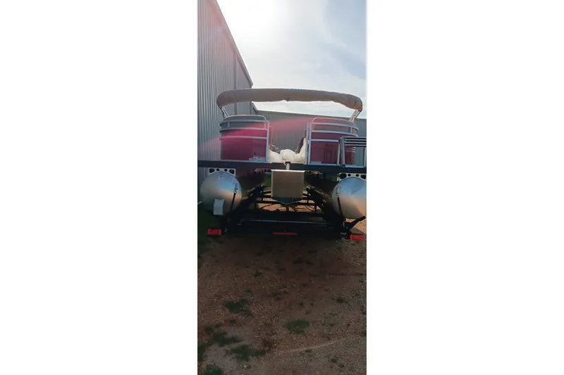 Slide: The Image of 2025 Sun Tracker Party Barge 24 DLX pontoon boat, rear view, parked outdoors. - 2