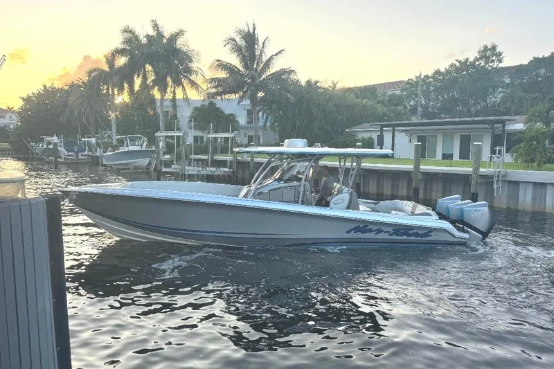 Slide: The Image of 2024 Nor-Tech 340 Sport boat cruising near a dock at sunset with palm trees. - 5