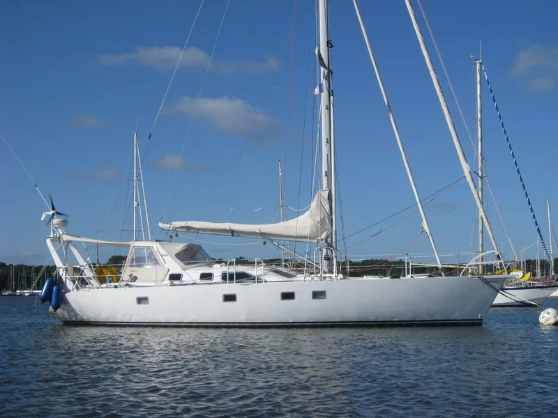 The Image of Eine weiße Segelyacht liegt ruhig im Wasser, umgeben von anderen Booten und einem klaren blauen Himmel. - 0