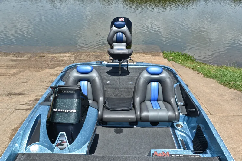 Slide: The Image of 2012 Ranger Z518 boat with blue and gray seats, docked by a lake. - 22