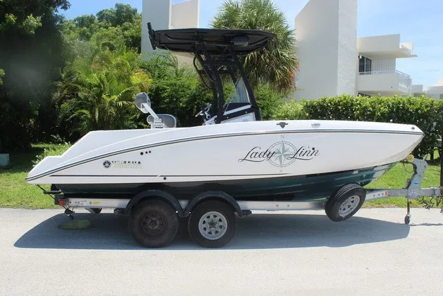 Slide: The Image of A 2021 Yamaha 210 FSH Sport boat on a trailer, surrounded by green vegetation. - 3