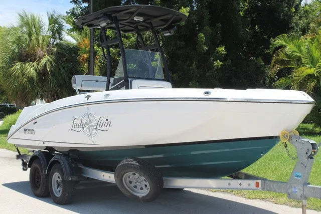 The Image of A 2021 Yamaha 210 FSH Sport boat on a trailer, surrounded by palm trees. - 1