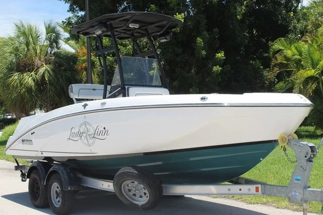 Slide: The Image of A 2021 Yamaha 210 FSH Sport boat on a trailer, surrounded by palm trees. - 2