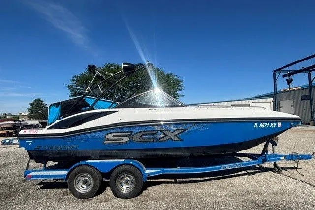 Slide: The Image of 2017 Starcraft SCX Surf 211 IO boat on trailer, blue and white design, sunny day. - 2