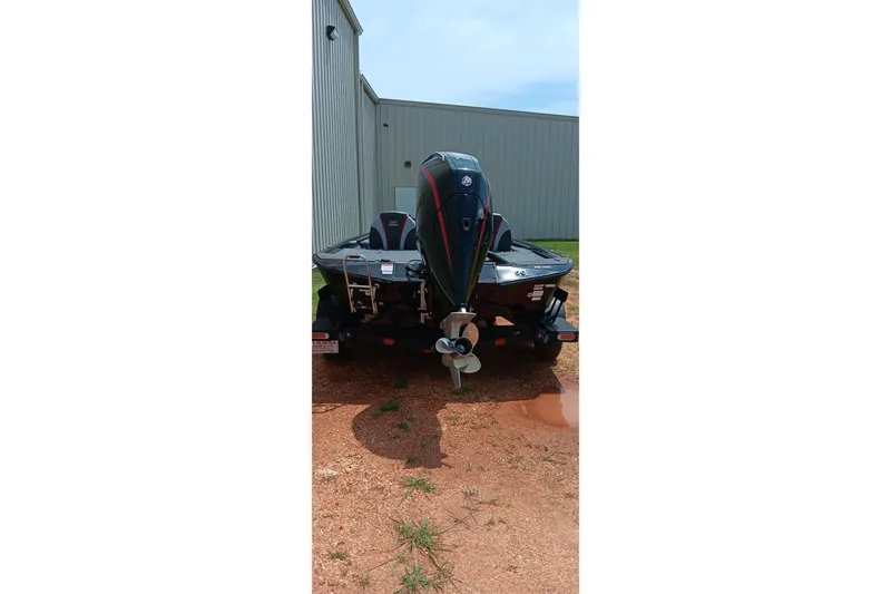 Slide: The Image of 2025 Ranger ALPHA 208 boat, rear view, parked on gravel near a metal building. - 2