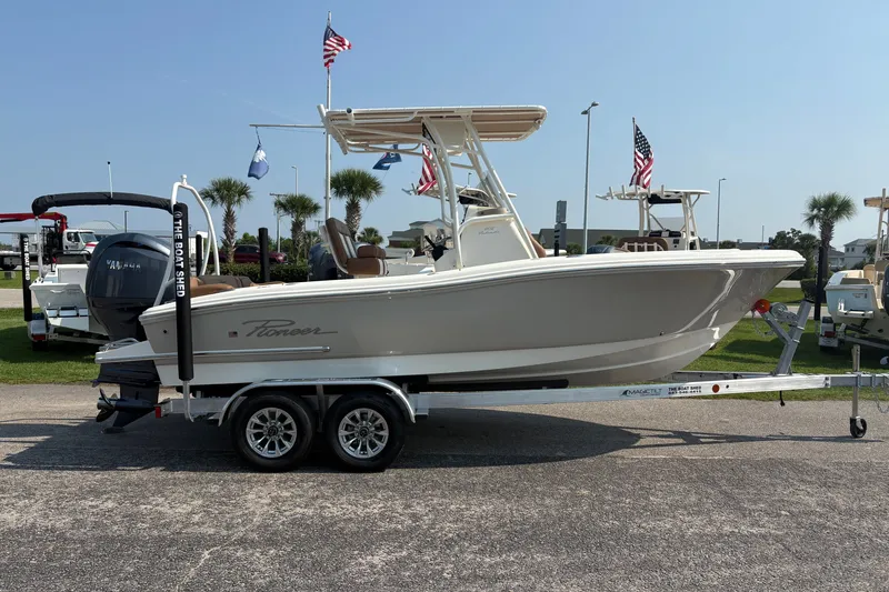 Slide: The Image of 2027 Pioneer 202 Islander boat on trailer, displayed outdoors with flags and palm trees. - 4