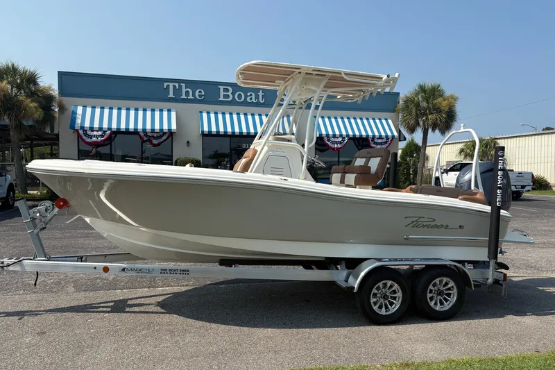 The Image of 2027 Pioneer 202 Islander boat on trailer outside dealership with striped awnings. - 0