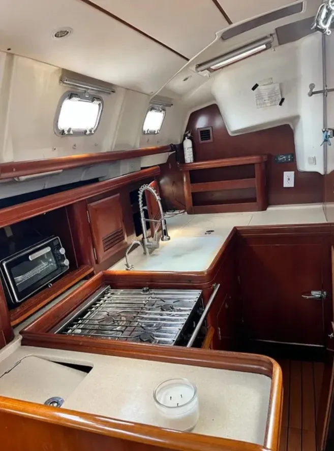 Slide: The Image of The galley of a 2005 Beneteau 423 with wooden cabinets, stove, and sink. - 10