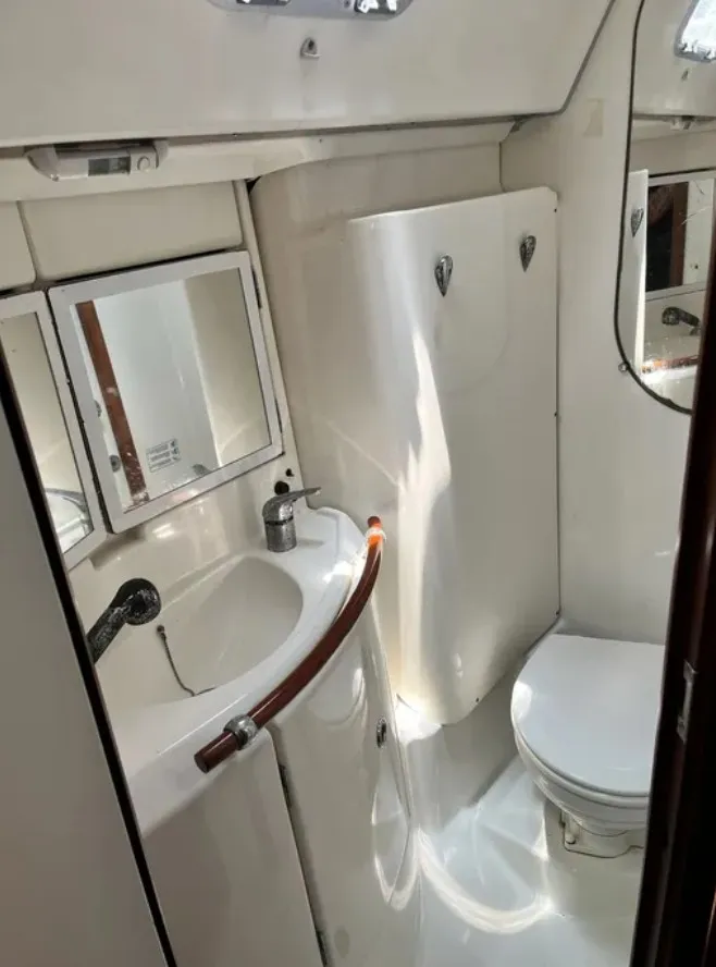 Slide: The Image of The image shows a clean, white bathroom on a boat with a sink, mirror, and toilet. - 14