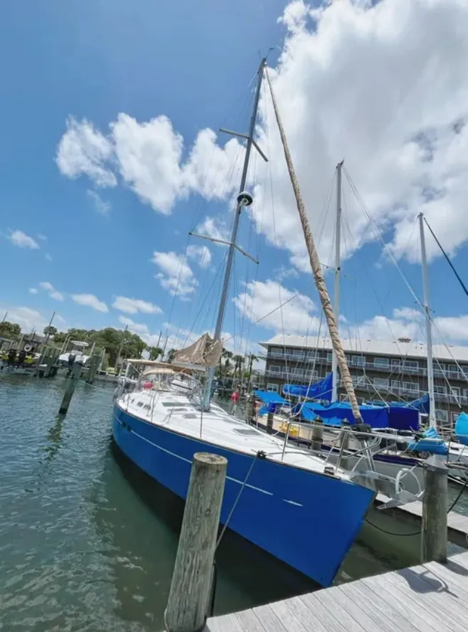 Slide: The Image of A blue sailboat is docked. The sky is clear with a few clouds. - 19