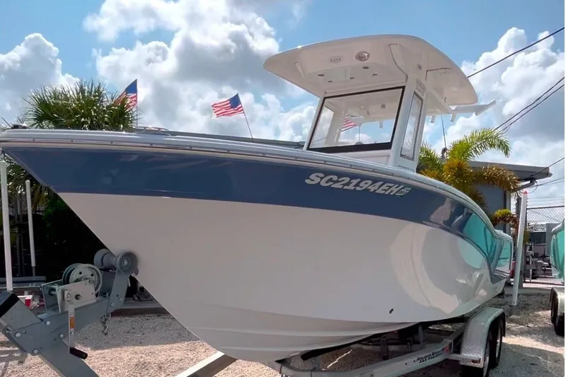 The Image of 2025 Sea Fox 228 Commander on a trailer, featuring a blue hull and T-top, under a blue sky. - 0