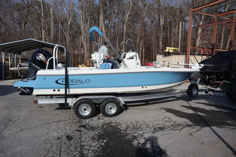 The Image of 2026 Robalo 226 Cayman boat on trailer, parked outdoors, featuring blue and white design. - 1