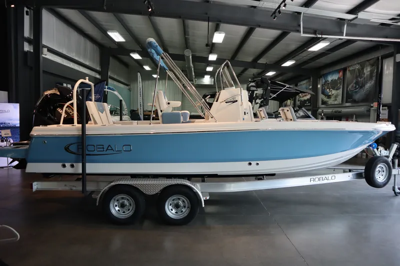 The Image of 2026 Robalo 226 Cayman boat in showroom, blue and white design on trailer. - 0