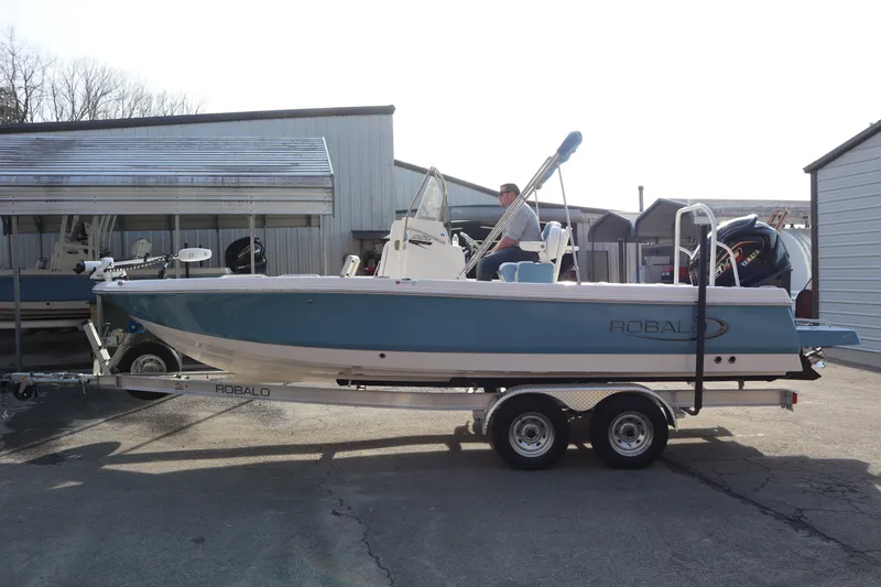 Slide: The Image of 2026 Robalo 226 Cayman boat on trailer, parked outdoors near storage buildings. - 3