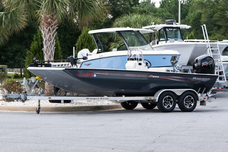Slide: The Image of 2022 Ranger RB200 boat on trailer, parked near palm trees and other boats. - 2