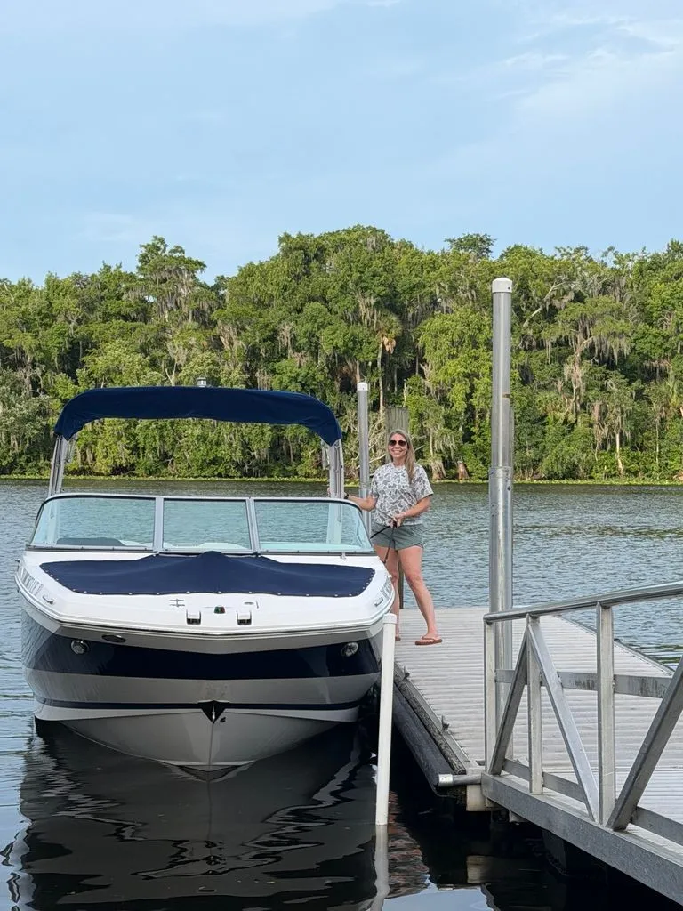 Slide: The Image of A woman stands on a dock next to a 2018 Regal 26 FasDeck boat. - 2