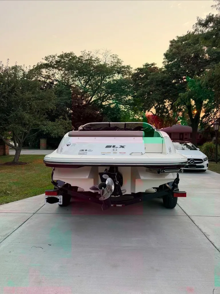 Slide: The Image of Rear view of a 2013 Sea Ray 210 SLX boat on a driveway, surrounded by trees. - 25