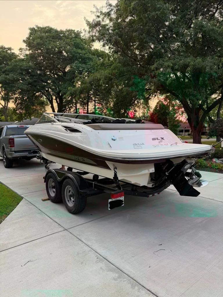 Slide: The Image of A 2013 Sea Ray 210 SLX boat on a trailer in a driveway, surrounded by trees. - 26