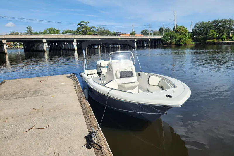 Slide: The Image of 2023 Tidewater 196 CC Adventure boat docked by a serene river under a clear sky. - 3