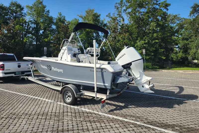 Slide: The Image of 2023 Tidewater 196 CC Adventure boat on trailer, parked in sunny lot with trees. - 7