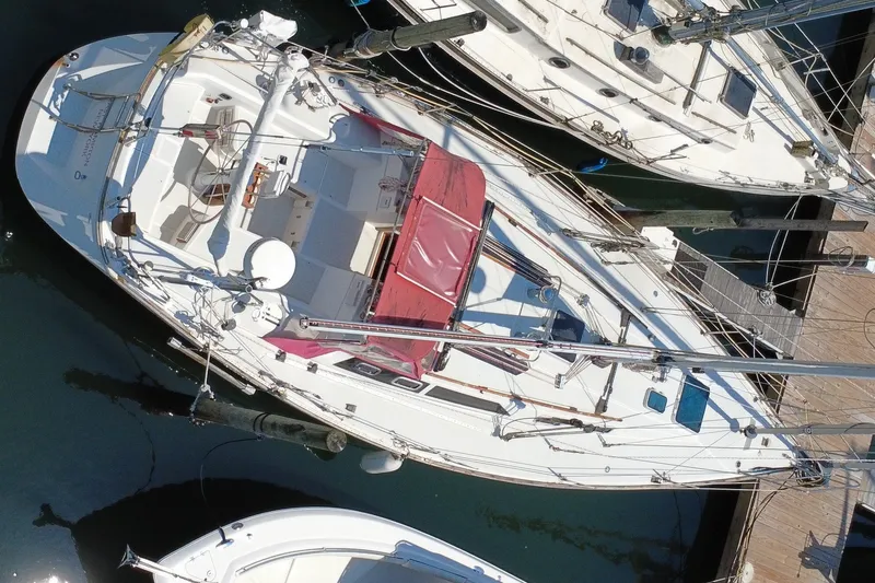 Slide: The Image of A sailboat with a red sunshade docked in a marina alongside other boats. - 7