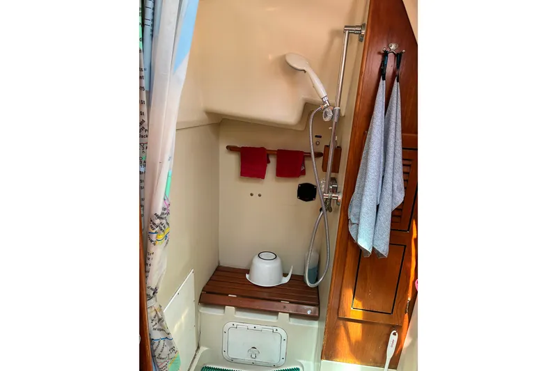 Slide: The Image of Compact shower area in a 1989 CAL 39 sailboat, featuring wooden bench and hanging towels. - 21