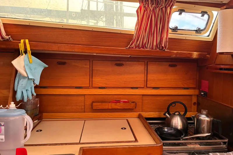 Slide: The Image of Cozy 1989 CAL 39 sailboat kitchen with wooden cabinets, kettle, and striped curtains. - 39