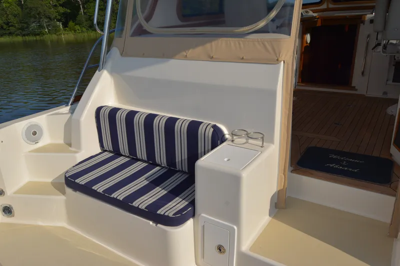 Slide: The Image of 2005 Sabre 38 Express boat with striped seating and wooden deck, docked by a serene lake. - 21