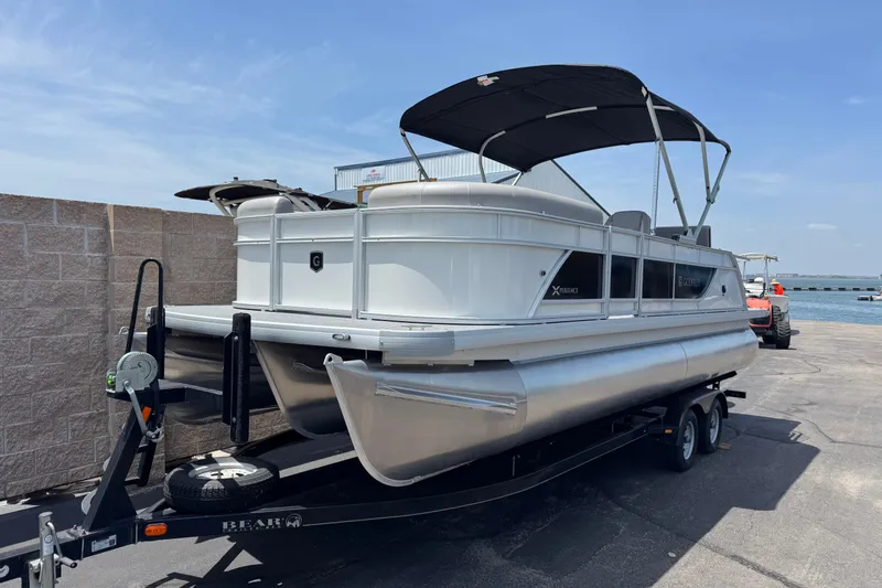 Slide: The Image of 2027 Godfrey Xperience 23' Lounger pontoon boat on trailer by the water. - 1