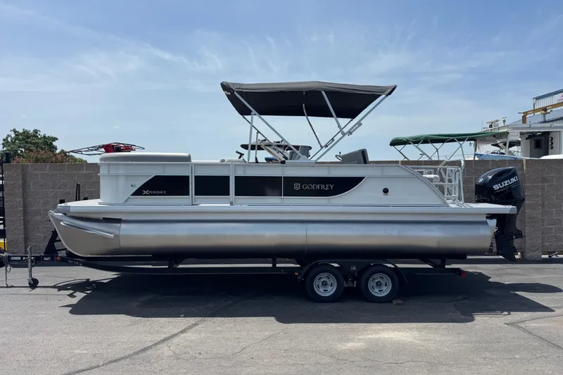 The Image of 2027 Godfrey Xperience 23' Lounger pontoon boat on trailer, featuring Suzuki outboard motor. - 0