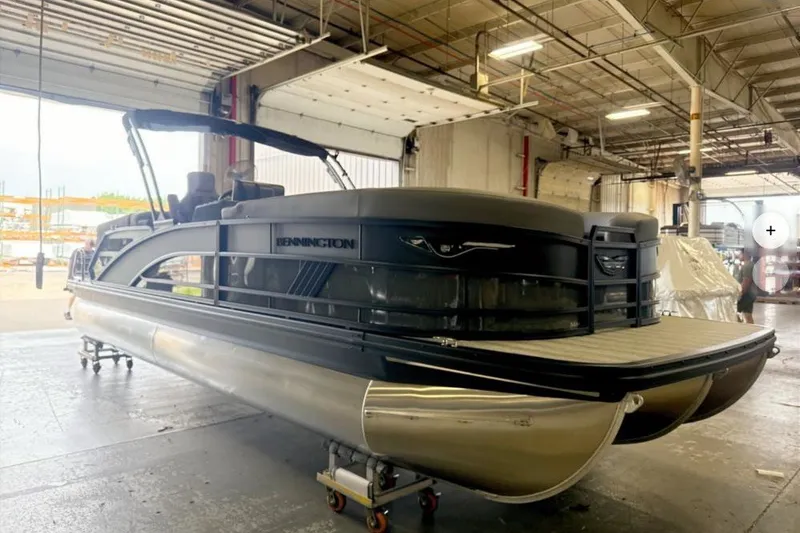 Slide: The Image of 2027 Bennington 24 M Open Fastback Quad Bench pontoon boat in a warehouse setting. - 0