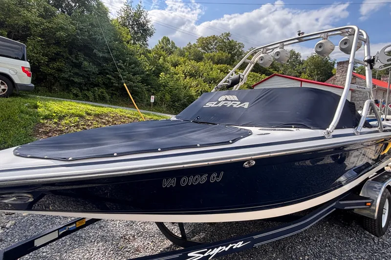 Slide: The Image of 2004 Supra Launch SSV boat on trailer, covered, parked outdoors with trees in background. - 2