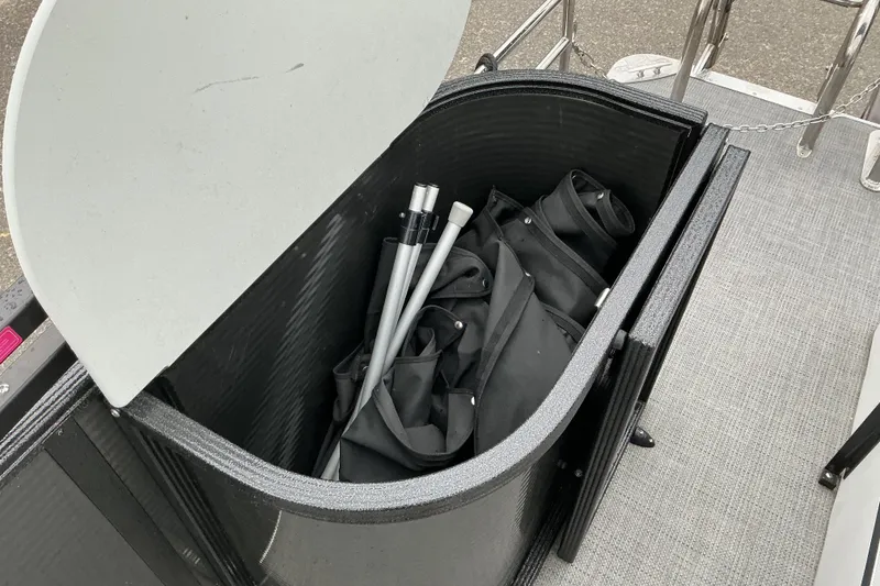 Slide: The Image of Open storage compartment on 2023 Crest Classic DLX 220 boat, containing folded black fabric and poles. - 13