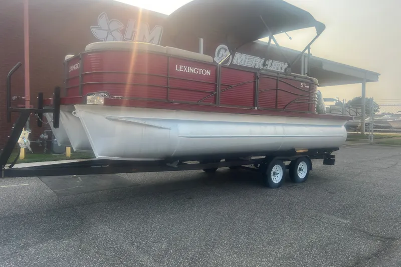 Slide: The Image of 2020 Lexington 521 pontoon boat on trailer, parked outdoors near a building. - 1