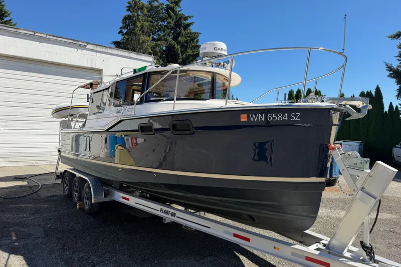 The Image of 2022 Ranger Tugs R-27 boat on trailer, parked outdoors near a white building. - 0
