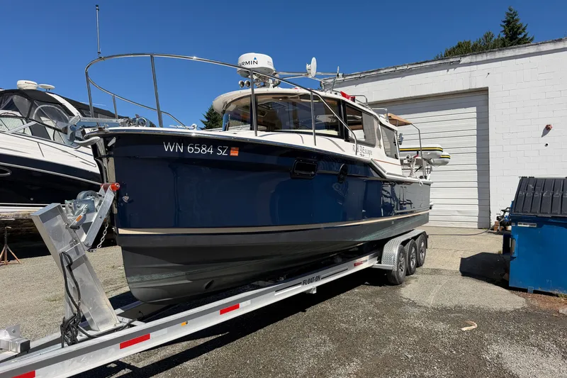 Slide: The Image of 2022 Ranger Tugs R-27 boat on trailer, parked outdoors near a white building. - 1