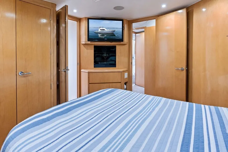Slide: The Image of Bedroom interior of 1999 Hatteras 60 Convertible yacht with striped bedding and wooden cabinetry. - 48