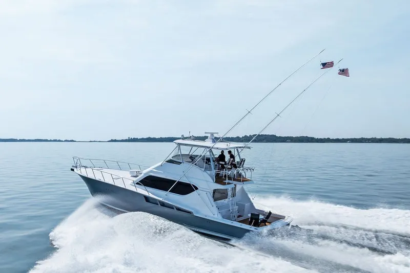 Slide: The Image of 1999 Hatteras 60 Convertible yacht cruising on calm waters with flags flying. - 13
