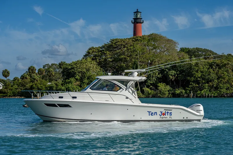 Slide: The Image of 2020 Pursuit OS 355 Offshore boat cruising near a lighthouse, surrounded by lush greenery. - 10