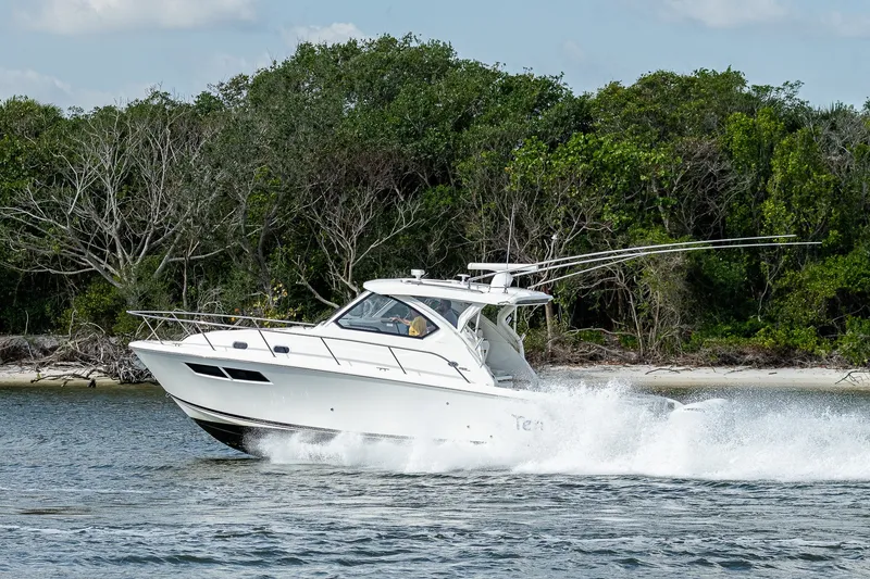 Slide: The Image of 2020 Pursuit OS 355 Offshore boat cruising near a lush, wooded shoreline. - 21