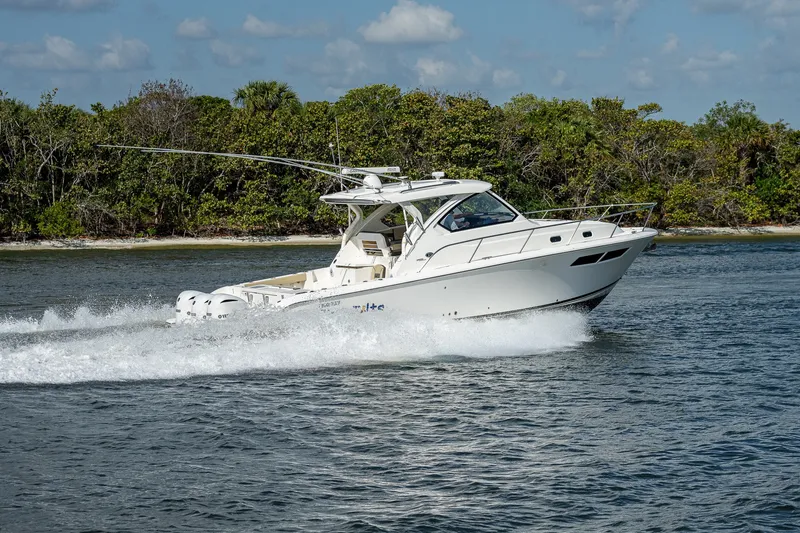 Slide: The Image of 2020 Pursuit OS 355 Offshore boat cruising on water near a forested shoreline. - 27