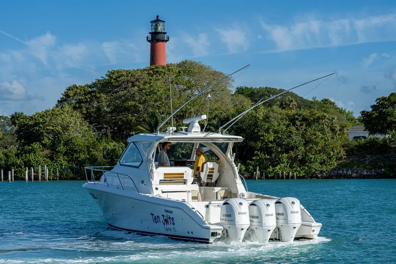 Slide: The Image of 2020 Pursuit OS 355 Offshore boat cruising near a lighthouse, surrounded by lush greenery. - 8