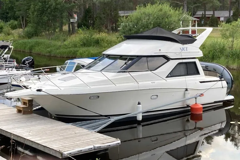 The Image of 1995 Bayliner 3258 Avanti yacht docked on a serene river with lush greenery. - 1