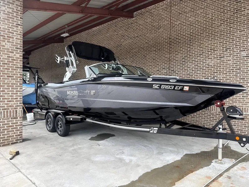 The Image of A black 2019 MasterCraft XT25 boat on a trailer in a covered area. - 1