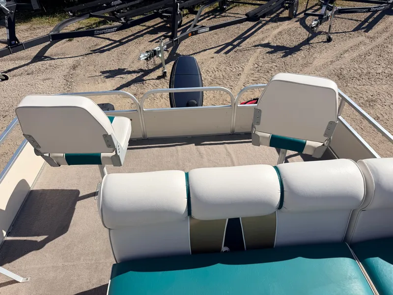 Slide: The Image of A pontoon boat with white and green seats, parked on a trailer. - 9