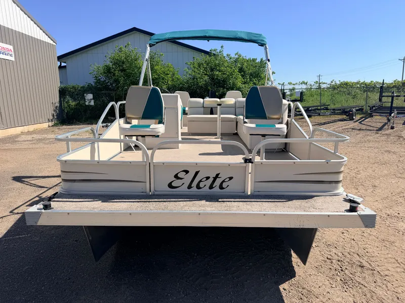 Slide: The Image of An Elete pontoon boat with seating and a sunshade, parked on dry land. - 38
