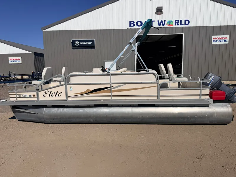 Slide: The Image of A 2006 Elete pontoon boat is on dry land in front of a boat dealership. - 44