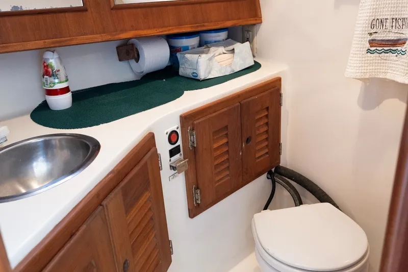 Slide: The Image of 2001 Carolina Classic 28 Express boat bathroom with sink, toilet, and wooden cabinets. - 12